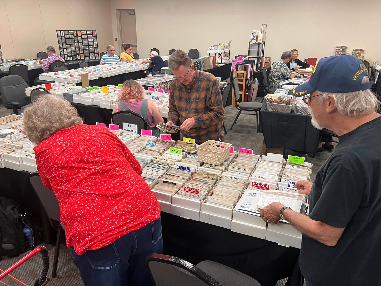 Collectors browsing tables of one-dollar postcards in labeled boxes.