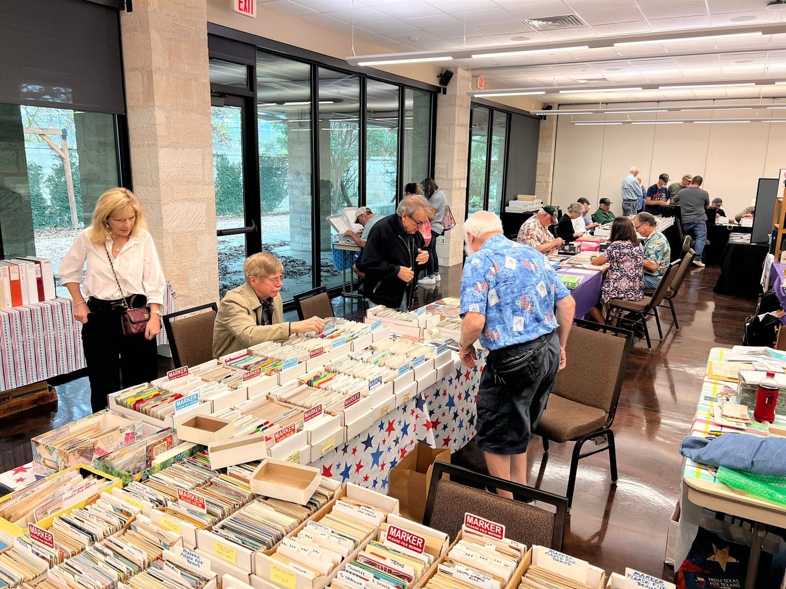 Collectors searching through postcard boxes on a star-patterned tablecloth.
