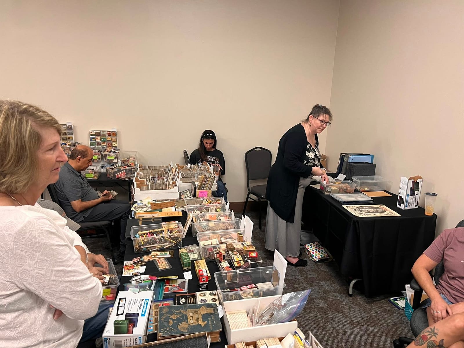 A table of matchbooks, vintage pens, and small paper collectibles in bins.